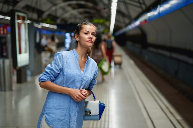 Mulher dentro do metrô esperando na plataforma de uma estação ferroviária para o trem chegar.