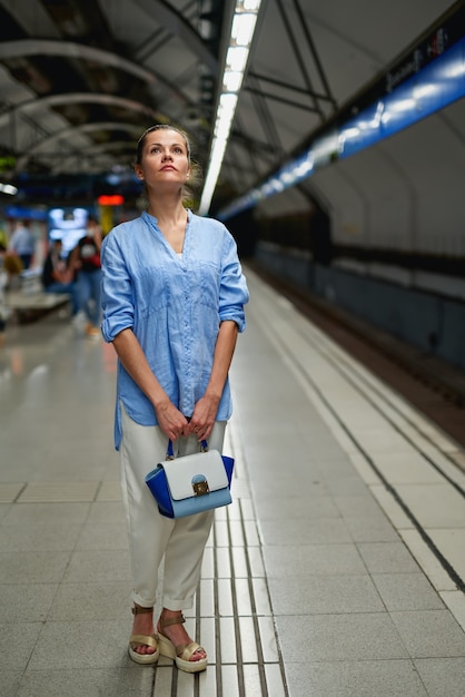 Mulher dentro do metrô esperando na plataforma de uma estação ferroviária para o trem chegar.