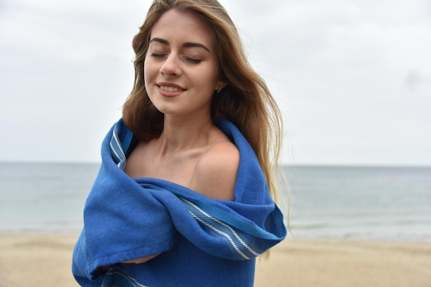 Mulher depois de nadar no mar envolto em toalha azul na praia na manhã nublada profundidade de campo rasa