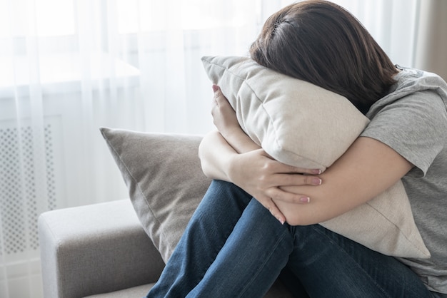 Mulher deprimida triste em casa sentado no sofá e abraçando um conceito de travesseiro, solidão e tristeza