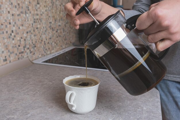 Mulher derrama café da prensa francesa em uma xícara de porcelana branca Preparando café moído em uma prensa