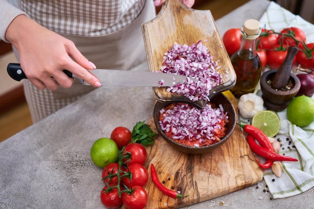 Mulher derramando cebola picada em tigela de madeira com tomate