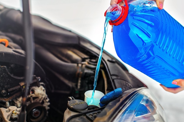 Mulher derramando líquido de lavagem de tela de carro anticongelante no carro sujo do recipiente de água anticongelante azul.