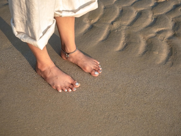 Mulher descalça em calças brancas com pernas dobradas em pé na praia tranquila sob a luz do sol quente ao pôr do sol à noite com espaço para cópia Destino de lazer de viagens de verão e conceitos de férias