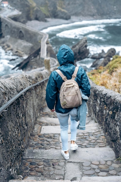 Mulher descendo as escadas de San Juan de Gaztelugatxe com uma capa de chuva