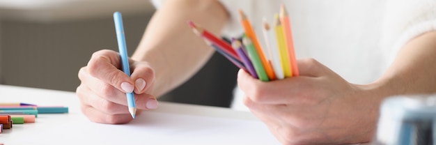 Mulher desenhando com lápis multicoloridos em uma folha de papel branca, close-up