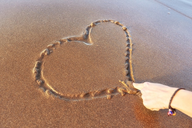 Mulher desenhando um coração na areia ao pôr do sol em um conceito de amor de verão.