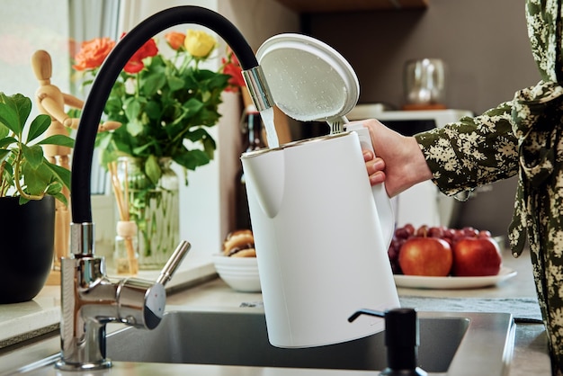 Foto mulher despejando água da torneira na chaleira elétrica na cozinha