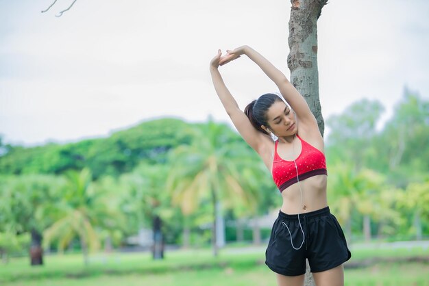 Mulher desportiva asiática esticando o corpo respirando ar fresco no parqueTailândia pessoasFitness e conceito de exercícioCorrer no parque