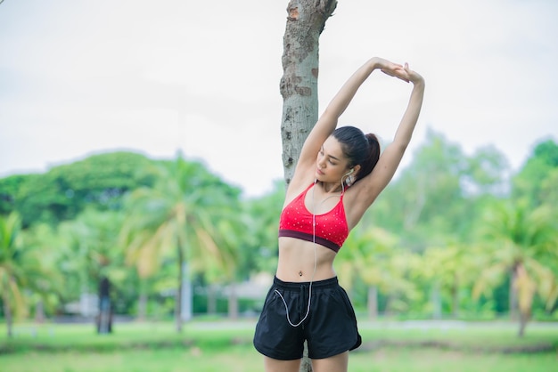 Mulher desportiva asiática esticando o corpo respirando ar fresco no parqueTailândia pessoasFitness e conceito de exercícioCorrer no parque