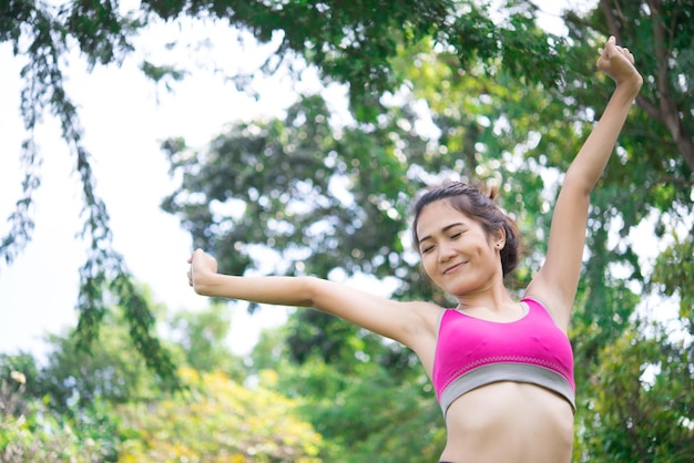 Mulher desportiva asiática esticando os braços respirando ar fresco no parquetailândia pessoas exercitam conceito