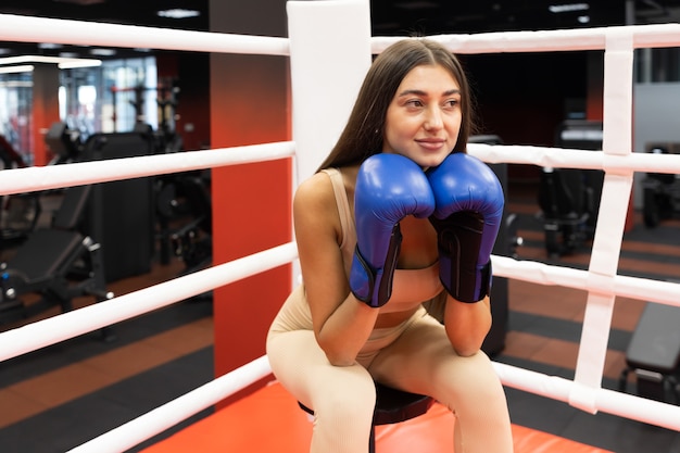 Mulher desportiva com luvas de boxe a descansar enquanto está sentada no ringue