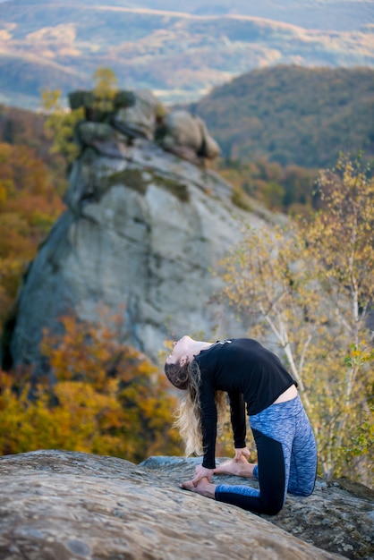 Mulher desportiva do ajuste está praticando ioga no topo da montanha