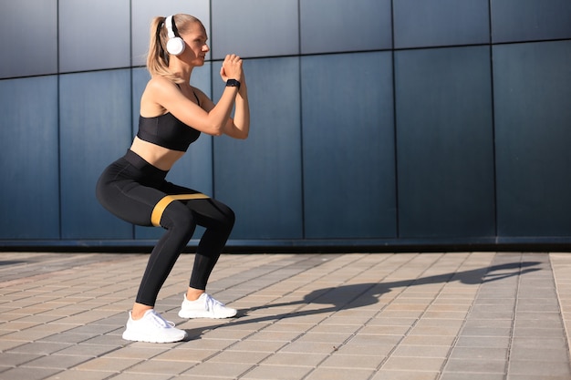 Mulher desportiva fazendo agachamento com expansor de goma de fitness ao ar livre.