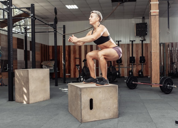 Mulher desportiva fazendo saltos de caixa no ginásio. Sportwoman pulando na caixa de madeira no clube de saúde cross fit.