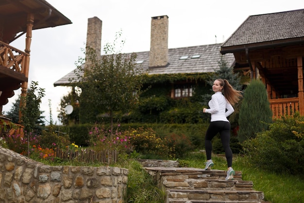 Mulher desportiva magra correndo lá em cima linda garota na trilha de treinamento em leggings e tênis de madeira