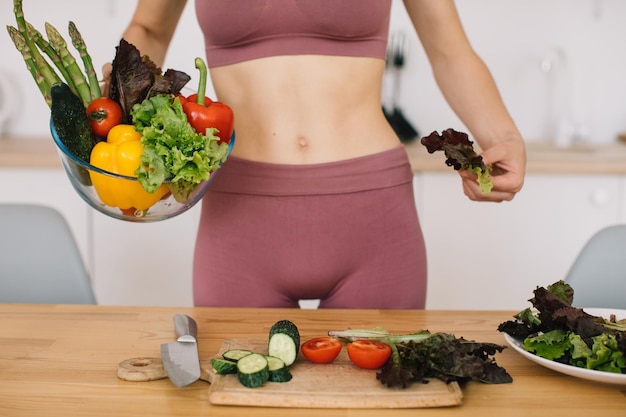 Mulher desportiva preparando salada de legumes fresca no conceito de alimentação saudável da cozinha
