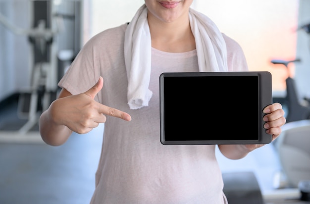 Mulher desportiva segurando um tablet vazio no ginásio de fitness. Bem-estar e saúde com tecnologia.