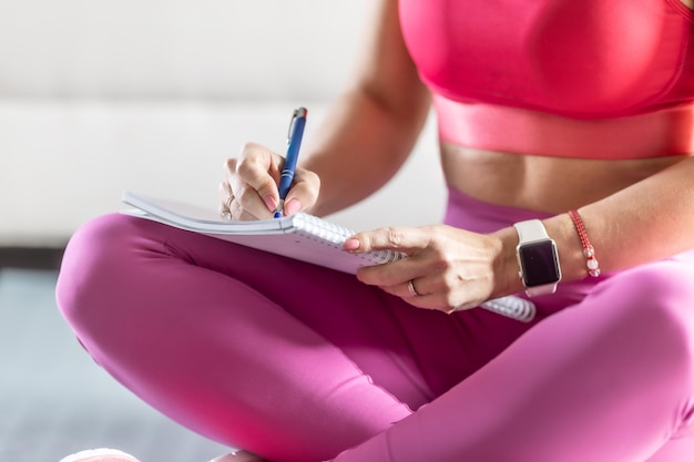 Foto mulher desportiva senta-se num tapete e escreve planos de treino futuros para alcançar resultados desportivos