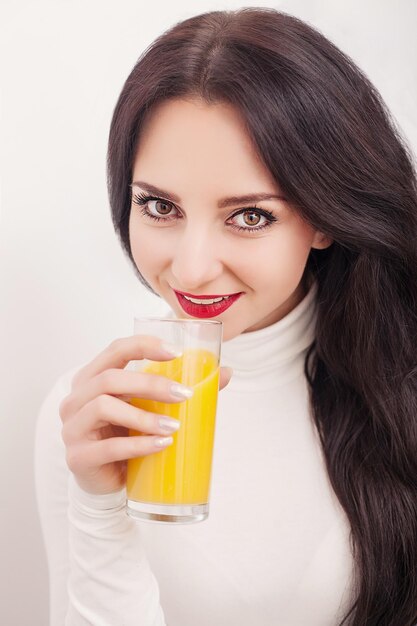 Mulher desportiva sobre fundo branco, segurando um copo de suco de laranja.