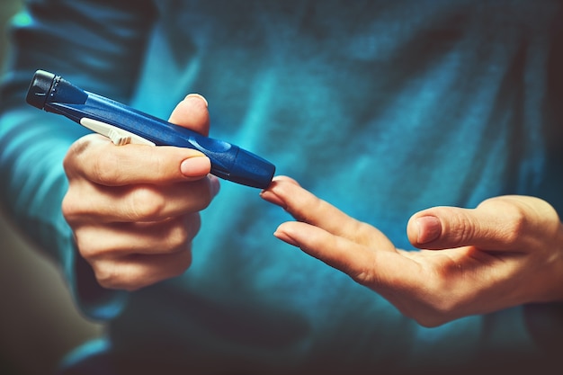 Mulher diabética usando medidor de glicose no sangue, mãos femininas segurando lanceta caneta glicosímetro no dedo medir açúcar verificar insulina