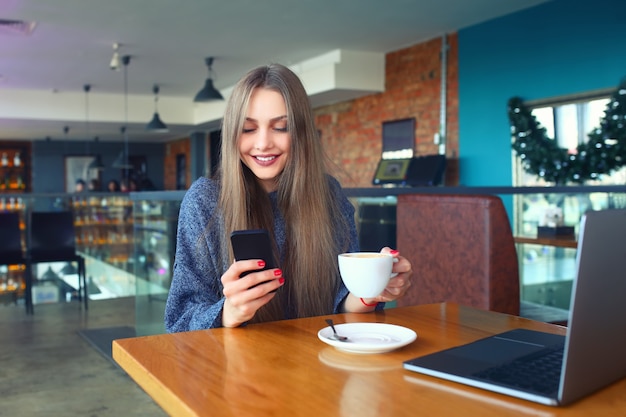 Mulher digitando a mensagem de texto no telefone inteligente em um café.