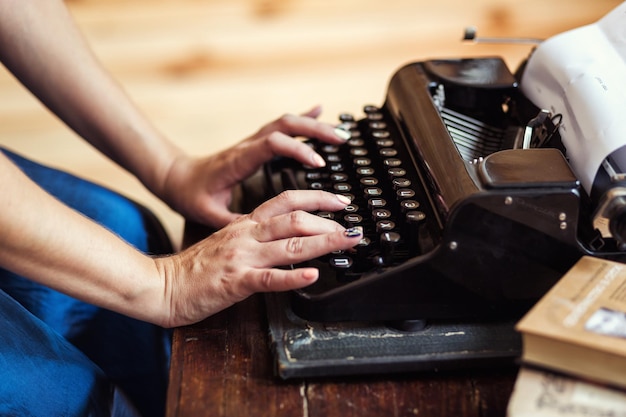 Mulher digitando na máquina de escrever vintage com papel em branco na mesa de madeira