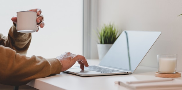 Mulher digitando no laptop enquanto bebe uma xícara de café