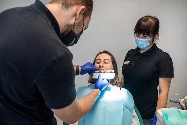 mulher discute branqueamento de dentes com seu dentista com um gráfico de amostra ao lado de seus dentes conceito de branqueamento de dentes seleção de tom de dente