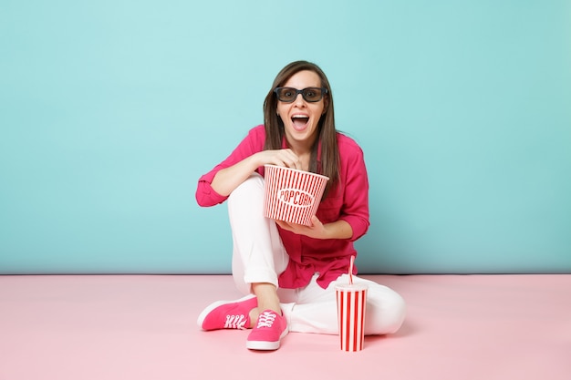 Mulher divertida de retrato de corpo inteiro com camisa rosa e calça branca sentada no chão assistindo filme