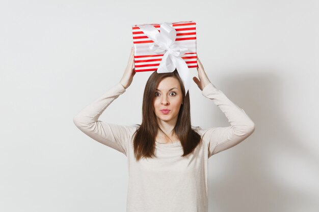 Mulher divertida segurando acima da cabeça uma caixa de presente listrada vermelha com fita isolada no fundo branco. Para propaganda. Dia de São Valentim, Dia Internacional da Mulher, aniversário de Natal, conceito de feriado