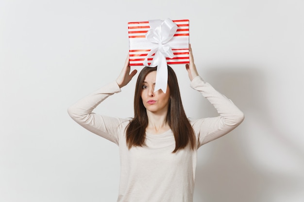 Mulher divertida segurando acima da cabeça uma caixa de presente listrada vermelha com fita isolada no fundo branco. Para propaganda. Dia de São Valentim, Dia Internacional da Mulher, aniversário de Natal, conceito de feriado