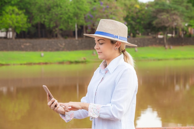 Mulher do agronegócio usando chapéu e jeans no final de um dia de trabalho segurando um celular