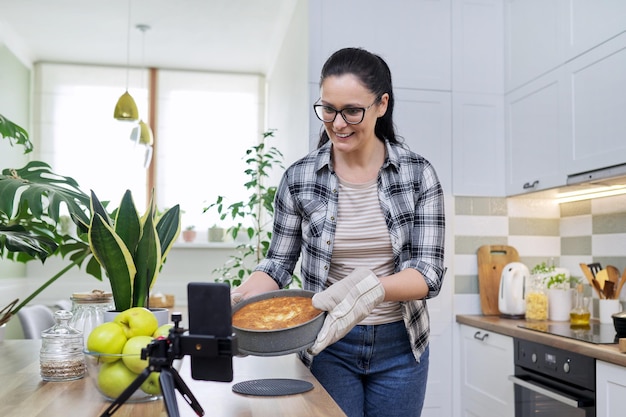 Mulher do blog de comida cozinhando torta de maçã em casa gravando receita no smartphone