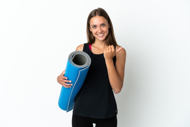 Mulher do esporte indo às aulas de ioga segurando um tapete sobre um fundo branco isolado apontando para o lado para apresentar um produto