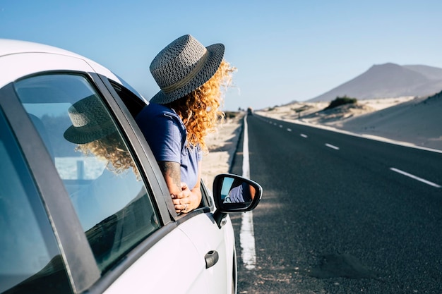 Foto mulher do lado de fora da janela do carro estacionado em uma longa estrada de asfalto durante a viagem viagem de verão