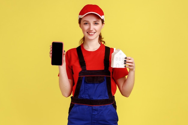 Mulher do motor mostrando o telefone inteligente da casa de papel com exibição em branco simulado para anúncio de reparo doméstico