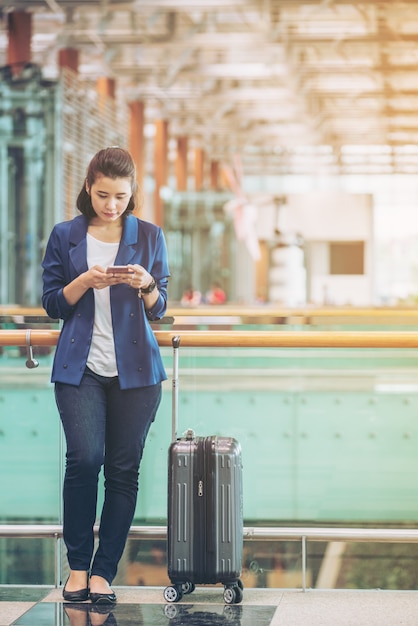 Mulher do turista com bagagem no aeroporto. Feliz jovem viajante com telefone celular.