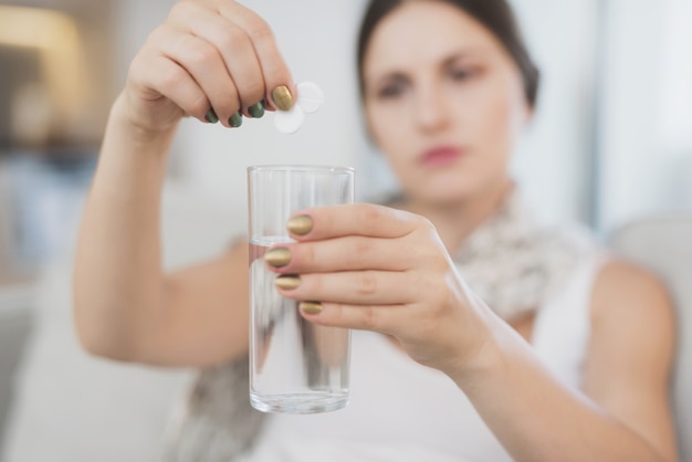 Mulher doente lança dois comprimidos em um copo de água.