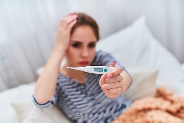 Mulher doente segura o termômetro na mão e o estica para a frente