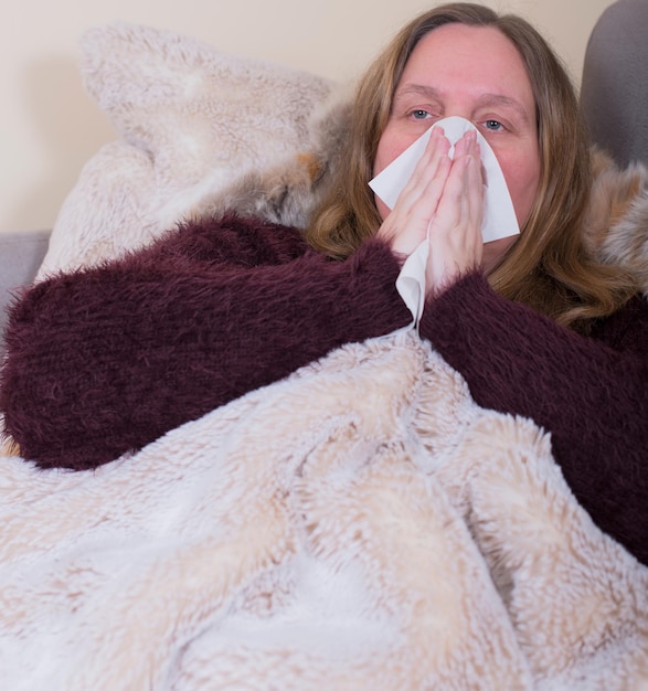 Foto mulher doente soprando o nariz enquanto se relaxa na cama em casa
