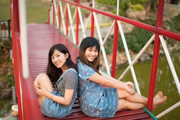 Mulher dois que relaxa na liberdade feliz de sorriso da ponte no parque com luz solar.