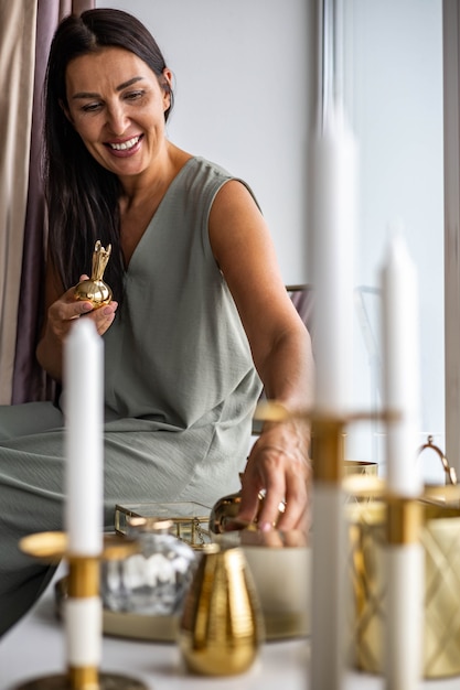 Mulher doméstica feliz coletando pratos vintage e decoração de interiores para casa sentada no parapeito da janela