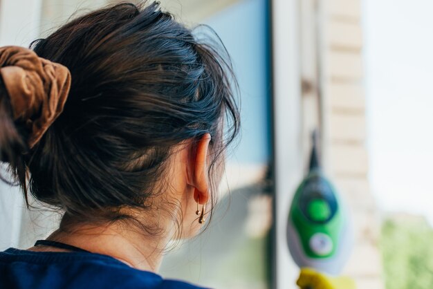 Mulher dona de casa com um dispositivo de vapor limpa a janela da sujeira.