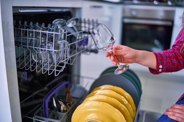 Mulher dona de casa usando máquina de lavar louça moderna para lavar pratos e copos na cozinha de casa