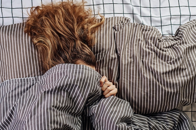 Mulher dormindo coberta com um cobertor na cama e despertador vintage no travesseiro.