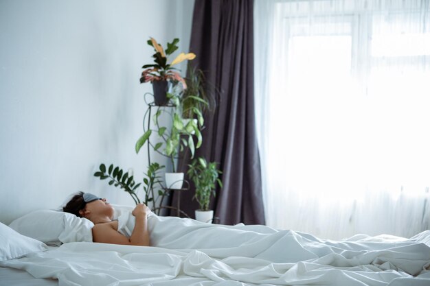 Mulher dormindo com máscara de dormir na cama com lençóis brancos