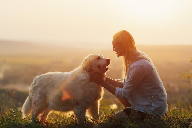 mulher e cachorro golden retriever sentam-se na grama verde ao pôr do sol