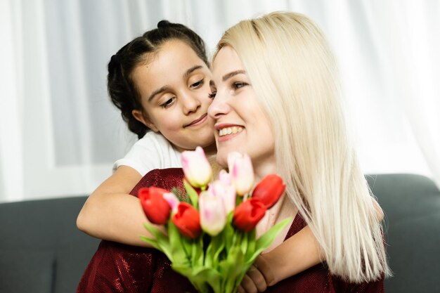 Mulher e criança com buquê de flores contra o fundo de casa. Conceito de férias em família de primavera. Dia da mulher.