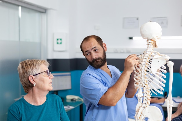Mulher e enfermeira olhando para a medula espinhal no esqueleto humano para exame osteopático. quiroprático apontando para os ossos da coluna para explicar o diagnóstico ao paciente aposentado para cuidados de saúde.
